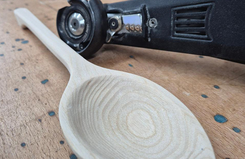 A hand-carved pale timber spoon with concentric tool marks in the bowl, beside a power carving tool