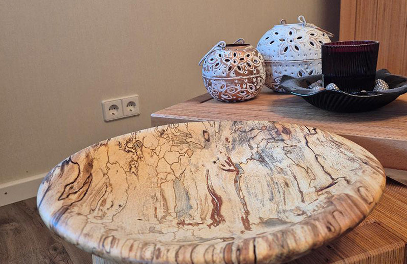 A shallow spalted timber bowl on a live-edge side table, beside two white ceramic lanterns